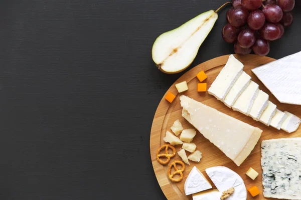 stock image Tasting cheese with fruits, pretzels and walnuts on dark background. Food for wine. Copy space. From above.