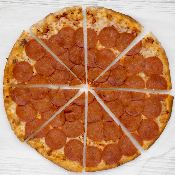 Leckere Pfefferoni-Pizza auf Pergament vor weißem Holzhintergrund, — Stockfoto