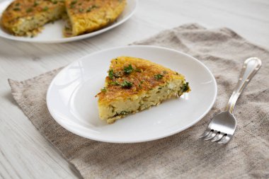 Beyaz bir tahta üzerinde beyaz bir tabakta bir parça spagetti omleti.