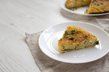 Beyaz bir tahta üzerinde beyaz bir tabakta bir parça spagetti omleti.