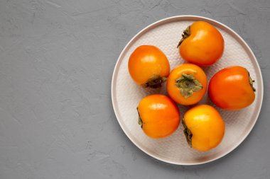 Çiğ olgun portakal hurmaları gri yüzey üzerinde bir tabakta, üst hayat