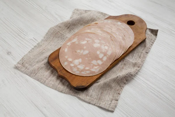 Sliced Mortadella Bologna Meat on a rustic wooden board on a whi