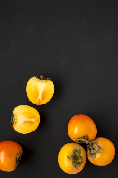 Raw maduro laranja caqui na superfície preta, vista superior. Depósito plano , — Fotografia de Stock