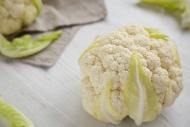 Çiğ Karnabahar Kafası beyaz ahşap bir yüzeyde, düşük açılı. 