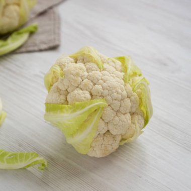 Çiğ Karnabahar Kafası beyaz ahşap bir arka planda, yan görünüm. 