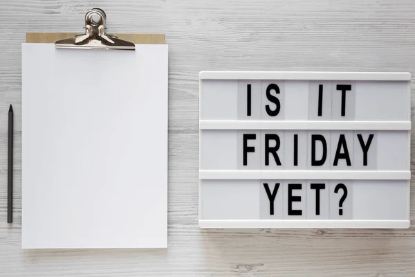 \'Is it friday yet?\' words on a lightbox, clipboard with blank sh