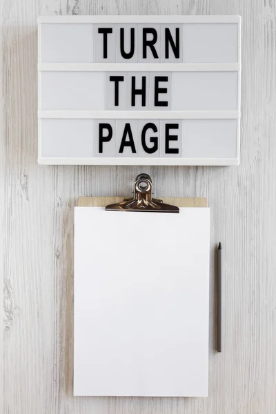 \'Turn the page\' words on a lightbox, clipboard with blank sheet