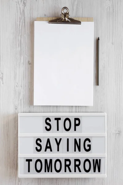 \'Stop saying tomorrow\' words on a lightbox, clipboard with blank