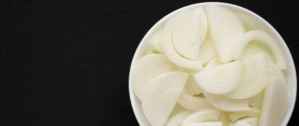 Cebollas blancas crudas picadas en un tazón blanco sobre una superficie negra, superior —  Fotos de Stock