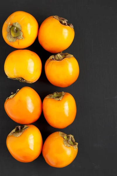 Raw maduro laranja caqui na superfície preta, vista superior. Depósito plano , — Fotografia de Stock