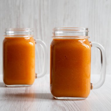 Ev yapımı Mango Havuç Smoothie cam kavanozlarda beyaz odunların üzerinde.
