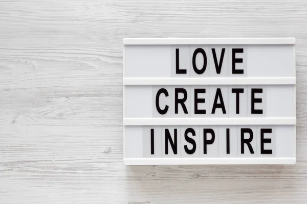 "Η αγάπη δημιουργεί έμπνευση" λέξεις σε ένα σύγχρονο πίνακα σε ένα λευκό ξύλινο — Φωτογραφία Αρχείου