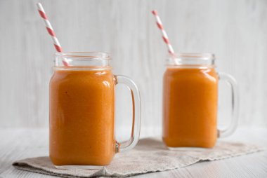 Ev yapımı Mango Havuç Smoothie cam kavanozlarda beyaz ahşap b