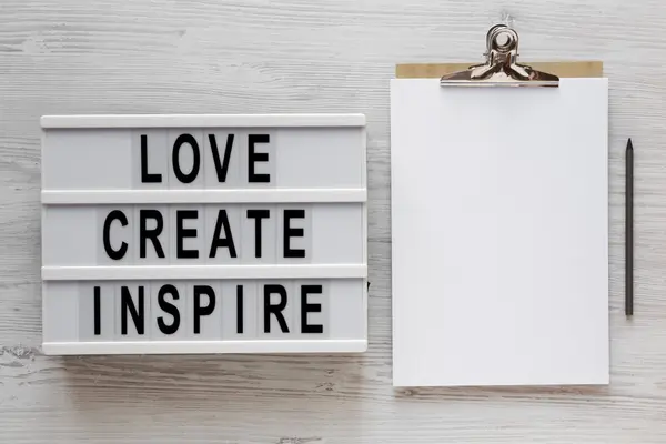 'Love create inspire' words on a lightbox, clipboard with blank — 스톡 사진