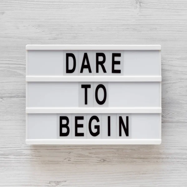 \'Dare to begin\' words on a modern board on a white wooden backgr