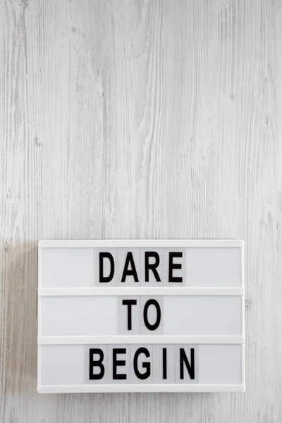 \'Dare to begin\' words on a lightbox on a white wooden surface, t