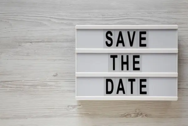 Mots "Save the date" sur une lightbox sur une surface en bois blanc, t — Photo