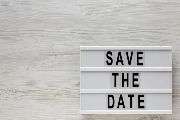 'Save the date' woorden op een lichtbak op een witte houten achtergrond — Stockfoto