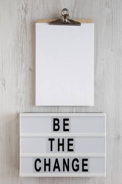 Işık kutusundaki 'Değişiklik ol' kelimeleri, boş sayfalı pano 