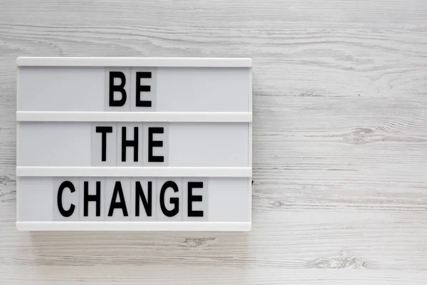 \'Be the change\' words on a lightbox on a white wooden surface, t