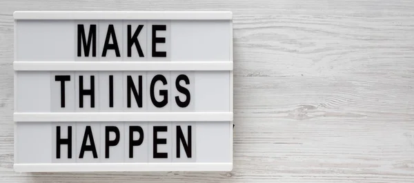 \'Make things happen\' words on a lightbox on a white wooden surfa