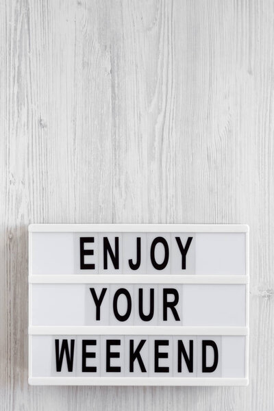 'Enjoy your weekend' words on a lightbox on a white wooden surface, top view. Overhead, from above, flat lay. Copy space.