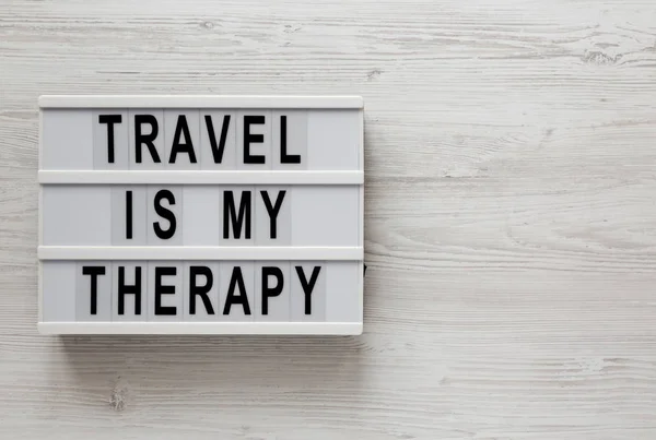 'Viajar é a minha terapia' palavras em uma caixa de luz em um branco sur de madeira — Fotografia de Stock