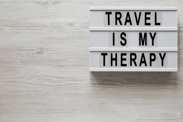 Viajar é a minha terapia. Palavras numa caixa de luz num bac branco de madeira. — Fotografia de Stock