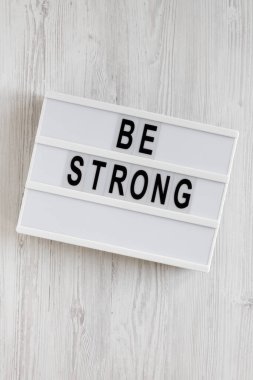 Beyaz ahşap bir arka planda, ışık kutusunda 'güçlü ol' kelimeleri