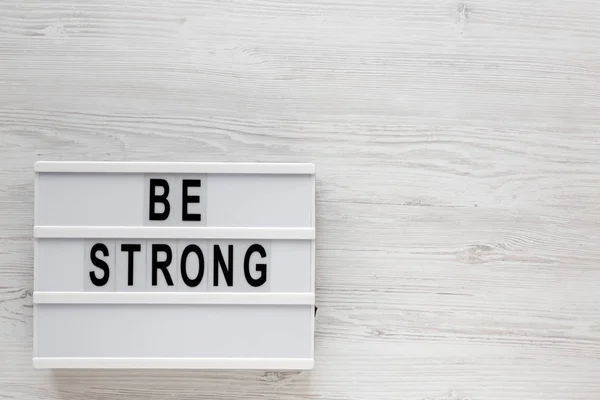 'Be strong' words on a lightbox on a white wooden surface, top v