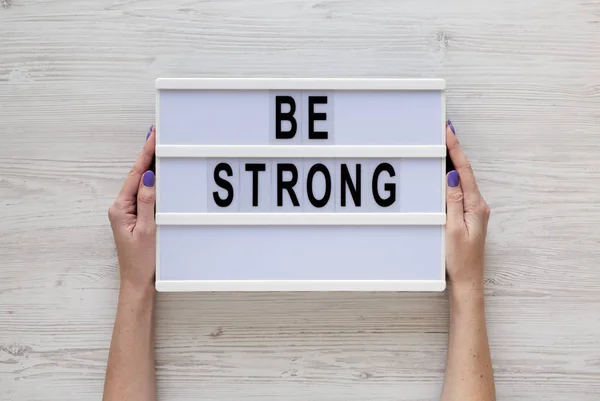 Female hands hold a lightbox with 'Be strong' words over white w — Stock Photo, Image