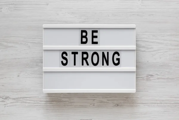 'Be strong' words on a lightbox on a white wooden background, to — Stock Photo, Image