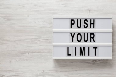 Beyaz ahşap bir yüzeyde ışık kutusunda 'Sınırlarınızı zorlayın' sözcükleri,