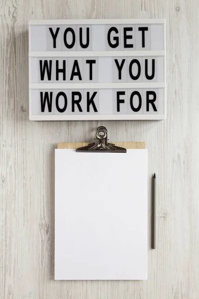 \'You get what you work for\' words on a lightbox, clipboard with