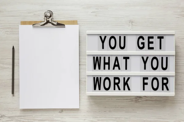 'You get what you work for' words on a lightbox, clipboard with