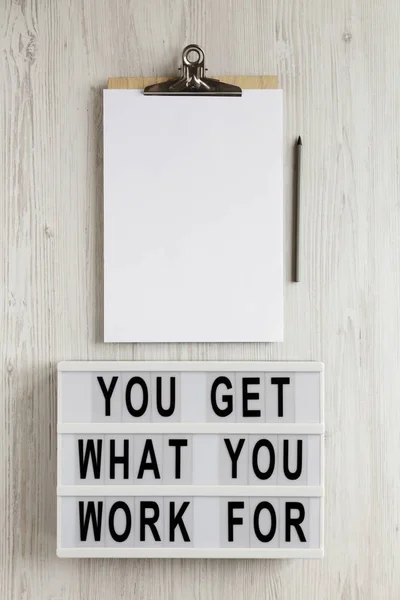 \'You get what you work for\' words on a lightbox, clipboard with