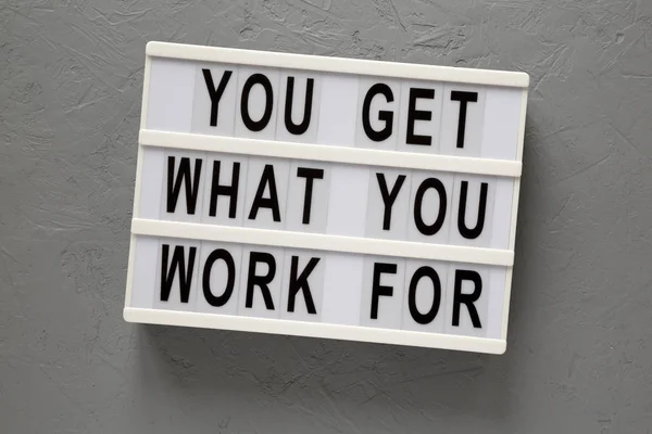 \'You get what you work for\' words on a lightbox on a gray surfac