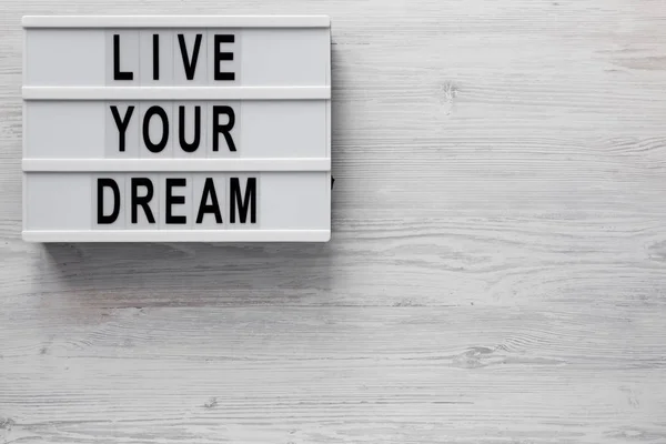 \'Live your dream\' words on a modern board on a white wooden back