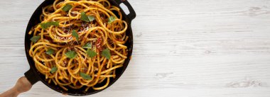 Ev yapımı Bucatini beyaz ahşap bir yüzey üzerinde dökme demir bir tavada bulunan Amatriciana Pasta. Dümdüz, tepede. Boşluğu kopyala.