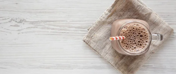 Ev yapımı New England çikolatalı milkshake, cam kavanoz bardakta, beyaz ahşap bir masada. Yukarıdan, dümdüz yatıyordu. Metin için boşluk.