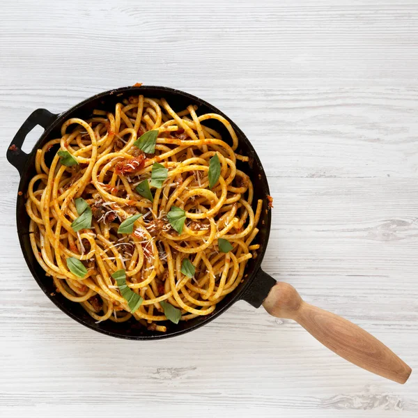 Homemade Bucatini all Amatriciana Pasta in a cast iron pan on a white wooden table, top view. Flat lay, overhead, from above.