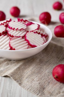 Taze Turp cipsleri beyaz ahşap arka planda beyaz bir kasede dilimler, düşük açılı görünüm. 