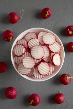 Beton arka planda beyaz bir kasede taze turp cipsi dilimleri, üst manzara. Dümdüz, tepeden, yukarıdan.