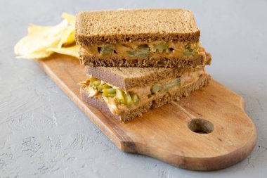 Ev yapımı Fıstık Ezmeli Sandviç, yanında patates cipsi ve beton arka planda ahşap bir tahta. Yakın plan..