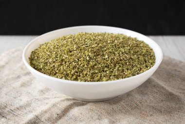 Kurumuş yeşil Yunan Oregano Baharatı beyaz bir kâse içinde, düşük açılı. Yakın plan..