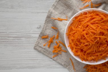 Beyaz ahşap zemin üzerinde beyaz bir kasede parçalanmış havuçlar, yukarıdan görüş. Düz yerde, üst tarafta, tepede. Boşluğu kopyala.