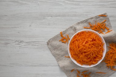 Beyaz ahşap bir masada beyaz bir kasede doğranmış havuçlar, üst manzara. Dümdüz, tepeden, yukarıdan. Metin için boşluk.