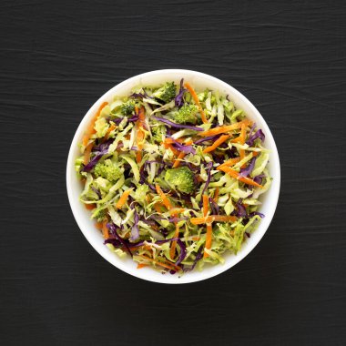 Ev yapımı çiğ brokoli salatası siyah bir yüzey üzerinde beyaz bir kasede, üst manzara. Dümdüz, tepeden, yukarıdan.