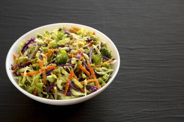 Homemade Raw Shredded Broccoli Slaw in a white bowl on a black surface, side view. Copy space. clipart