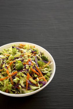 Ev yapımı çiğ brokoli salatası siyah bir yüzey üzerinde beyaz bir kasede, düşük açılı. Boşluğu kopyala.